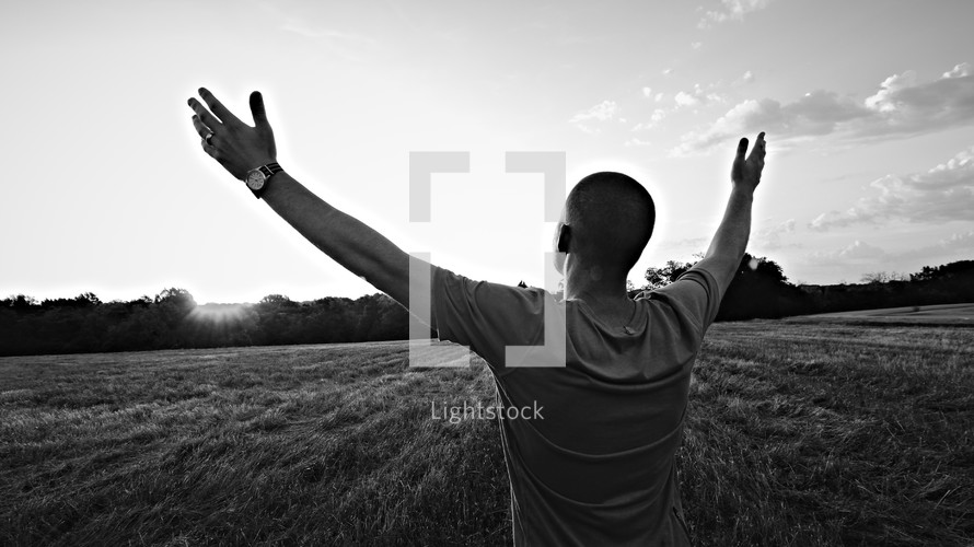 Man in field worshipping at sunrise