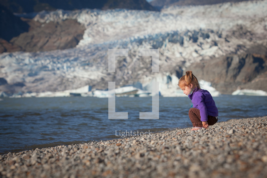 red head toddler squatting on a beach 