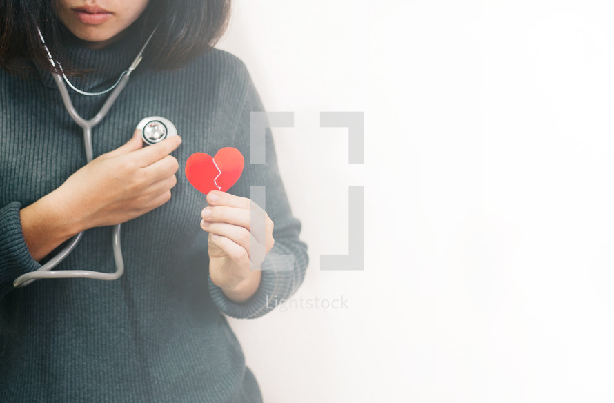 a woman holding a broken heart listening to her own heart with a stethoscope 
