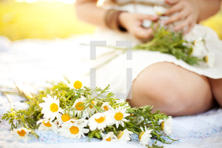 a woman sitting on a blanket with daisies 
