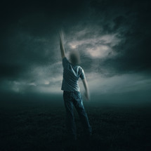 man standing with one arm raised, reaching up to the sky, storm clouds in the distance