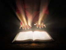 A woman with outstretched hands over an open Bible from which light shines.