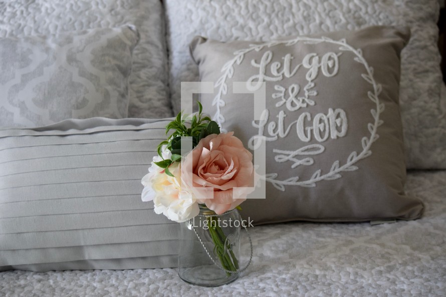 flowers and a Let Go and Let God throw pillow on a bed 