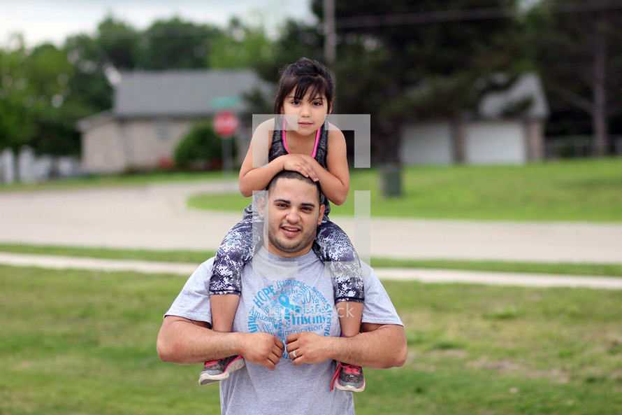 father with daughter on his shoulders standing outdoors