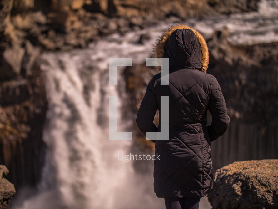 a woman in a coat looking out at a waterfall 