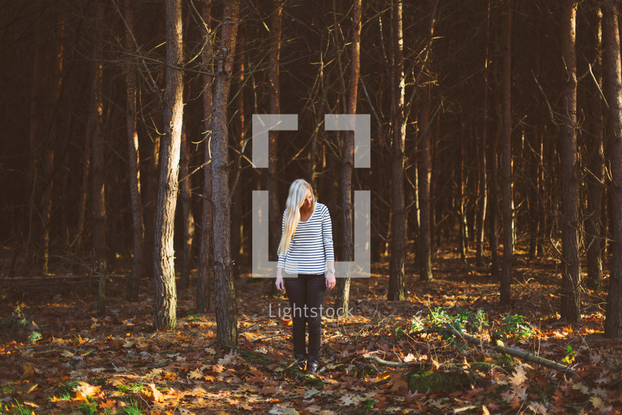 blonde woman standing alone in a forest 
