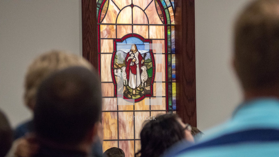 parishioners and a stained glass window of Jesus the good shepherd 