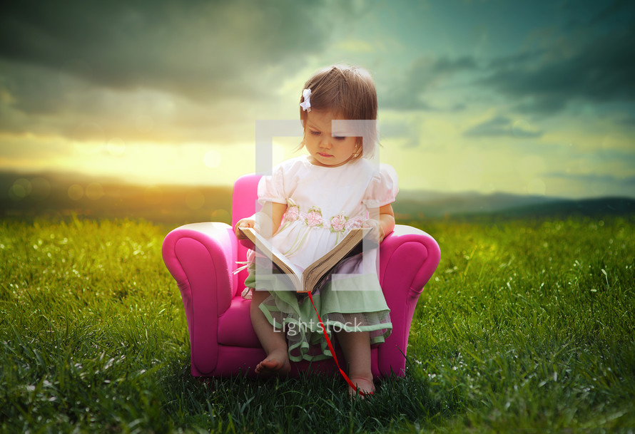 a little girl reading a Bible in a pink chair outdoors 