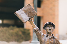 statue of a boy holding up a newspaper 