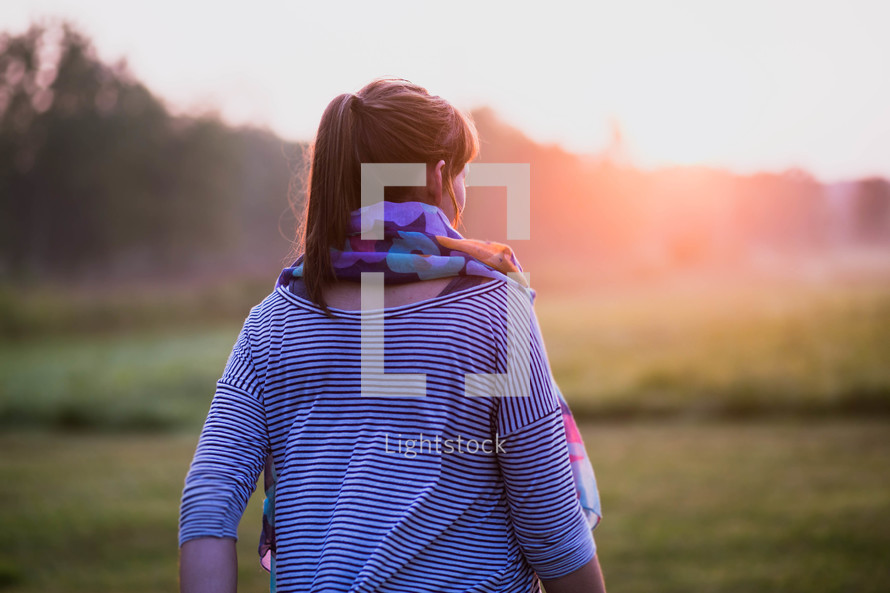 a woman in a scarf walking outdoors at sunrise 