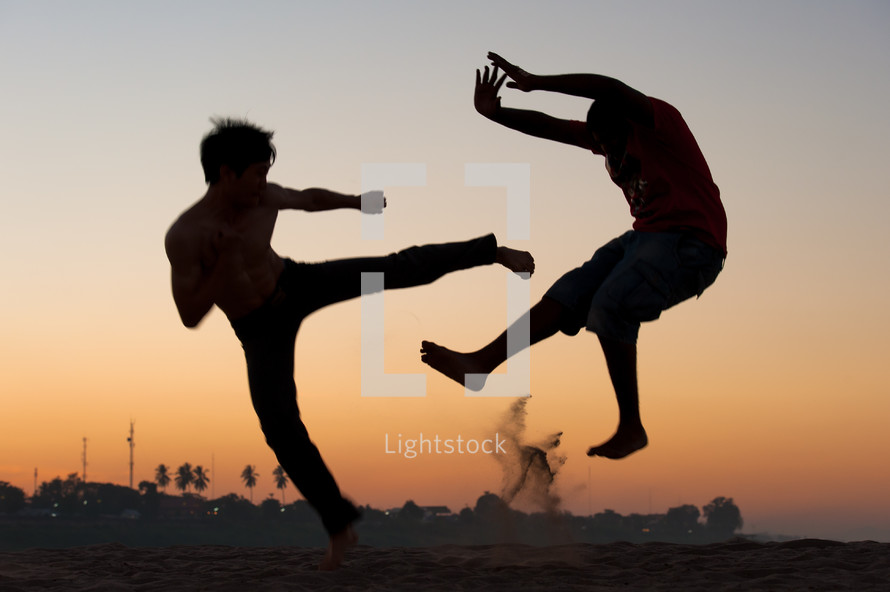 Silhouette of boys engaging in martial arts moves outside at dusk.