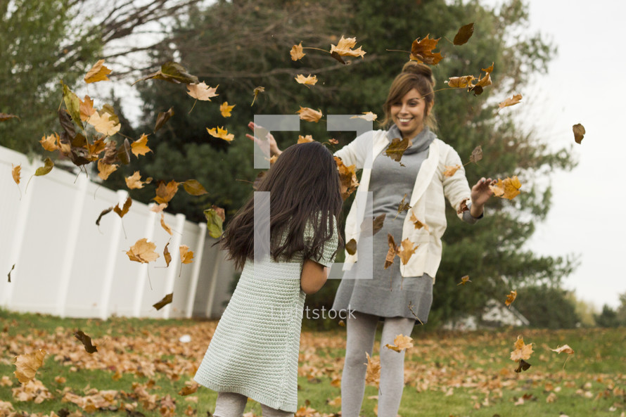 Mother and daughter playing in the fall leaves in the back yard.
