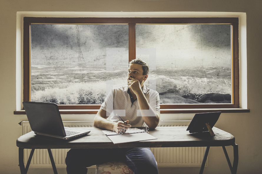 a man sitting at a desk with a raging storm at sea behind him 