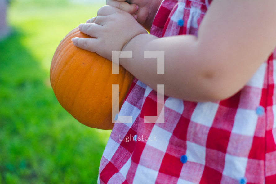 a toddler carrying a small pumpkin