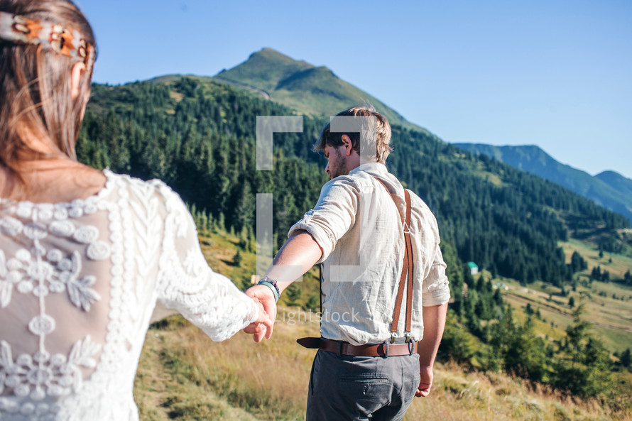 bride and groom holding hands walking through a mountain landscape 