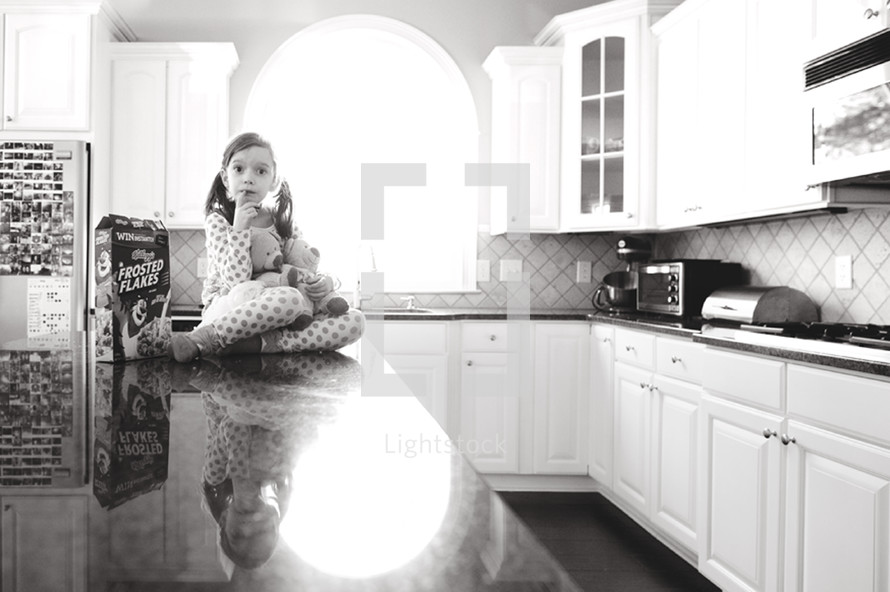 a girl child in pajamas sitting on a kitchen counter 