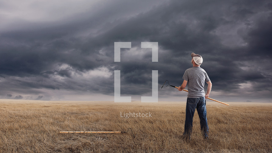 farmer holding a rake and looking up at storm clouds 