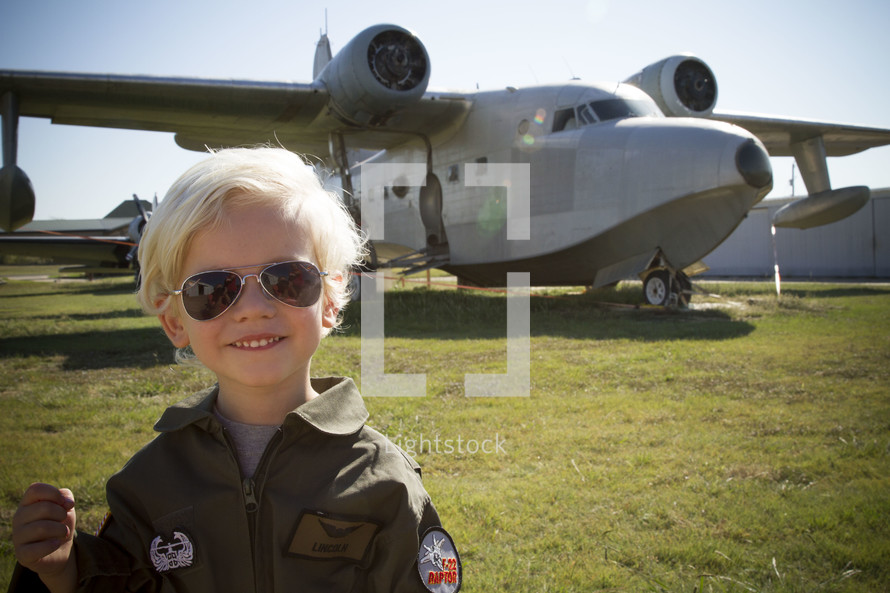a boy child in a fighter pilot outfit in front of a bomber