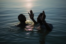 Baptism. Silhouette of two young black men in worship in the water at sunset