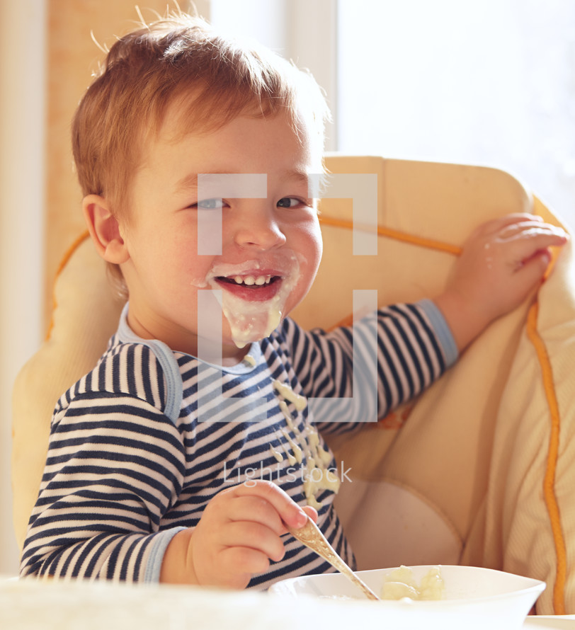 Two year old boy smiles and eating porridge