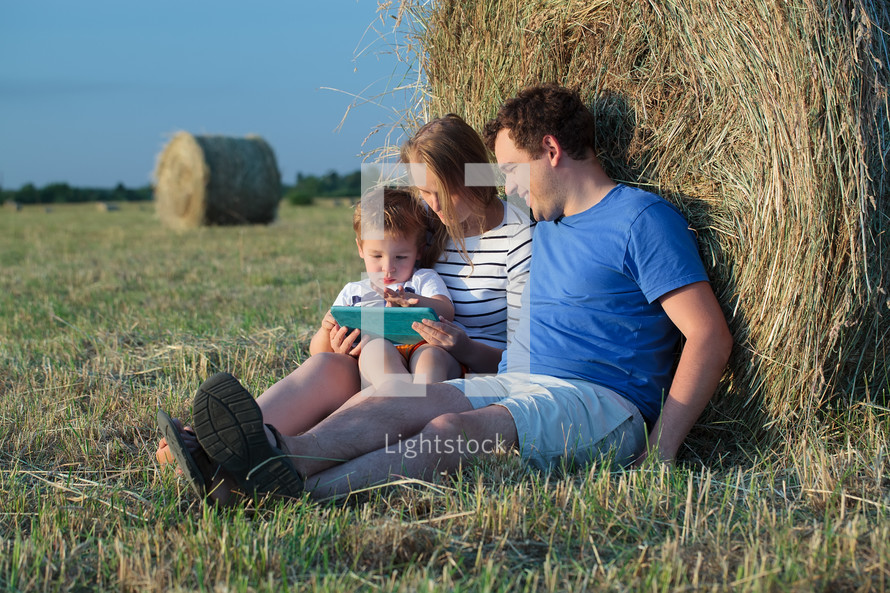 Family of three with pad in the field with hay rolls