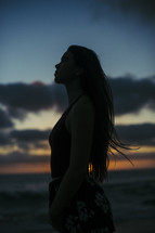 side profile of a woman standing on a beach at dusk 