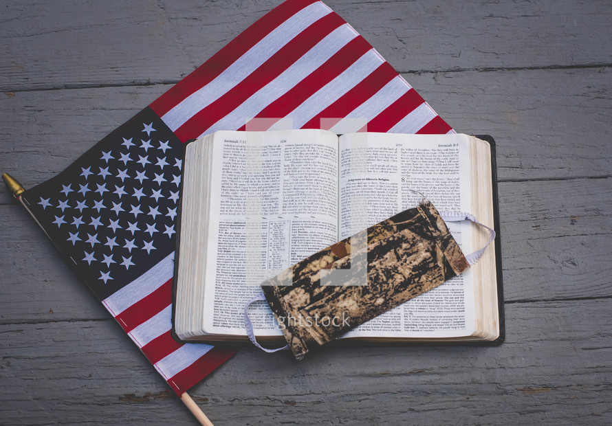 camouflaged mask on the pages of an opened Bible on an American Flag 