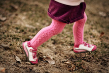 A little girl running in pink tights.