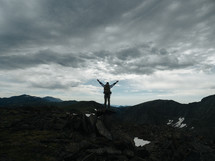 man standing on a mountaintop with raised arms 