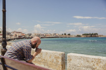 man in prayer sitting on a bench at the coast in Greece