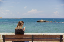 woman saying a prayer sitting on a bench on a beach in Greece 