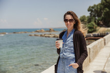 woman walking with a coffee cup along the coast in Greece 