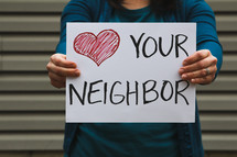 A woman holding a sign that reads love your neighbor.