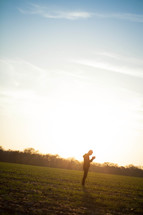 silhouette of a man in a field with his head bowed in prayer