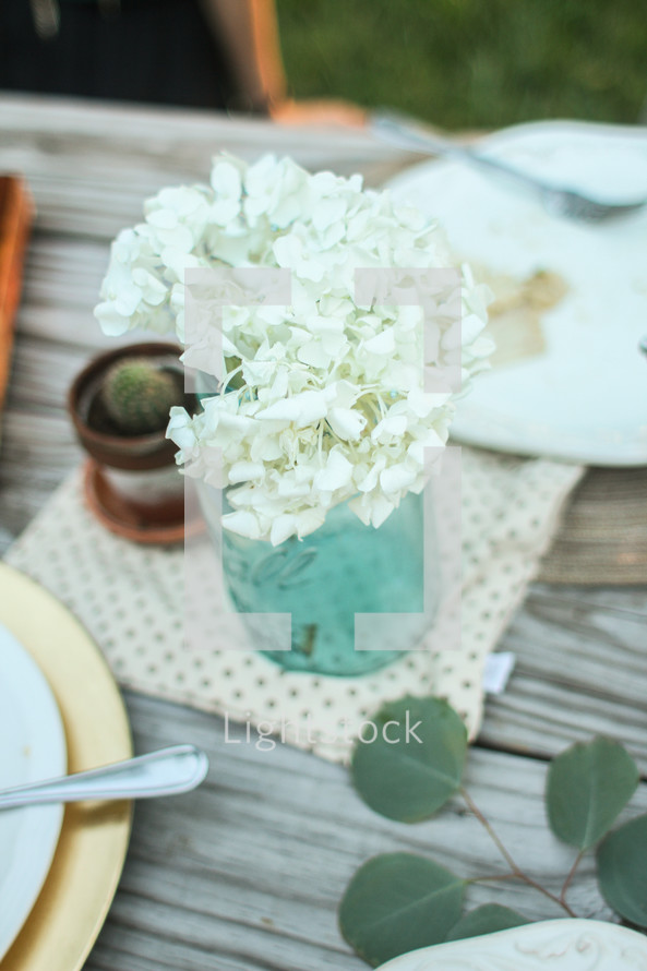 Mason jar of flowers on a picnic table outside.