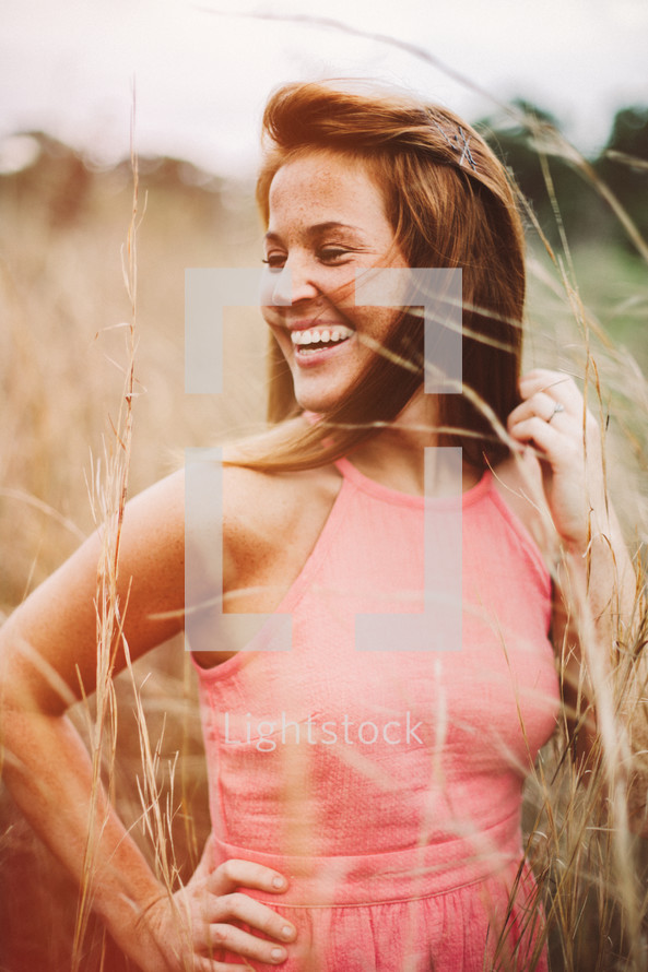 A smiling young woman in a field of tall grass.