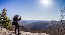 a backpacker on a mountaintop taking a picture 