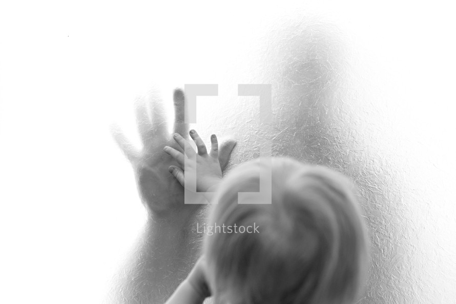 a child touching a parent's hand through frosted glass