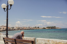 man in prayer sitting on a bench along the coast in Greece