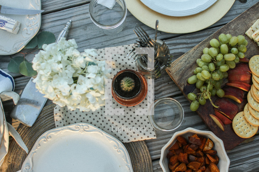 Place settings with fruits, nuts and flowers on a picnic table outside.