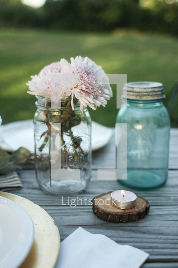 Flowers in a mason jar on a picnic table outside.