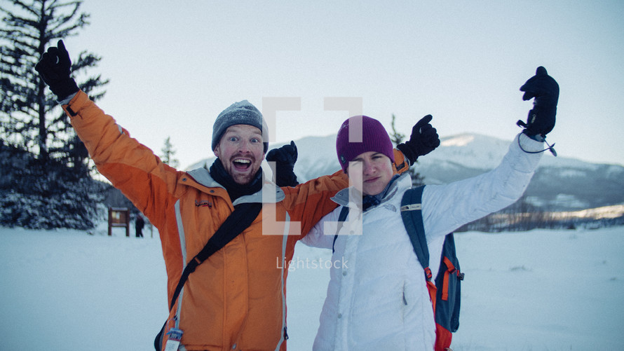 a couple in winter gear with arms raised 