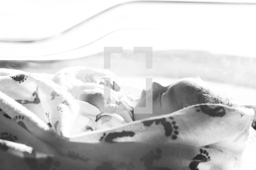 A sleeping newborn baby in a hospital crib.