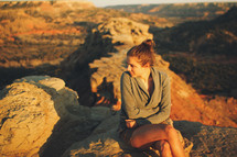 a woman sitting in a rocky desert landscape 