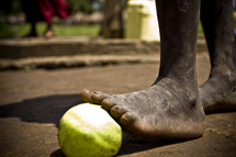 An apple rests under a dirty foot. 