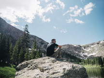 man sitting on a rock near a mountain lake 