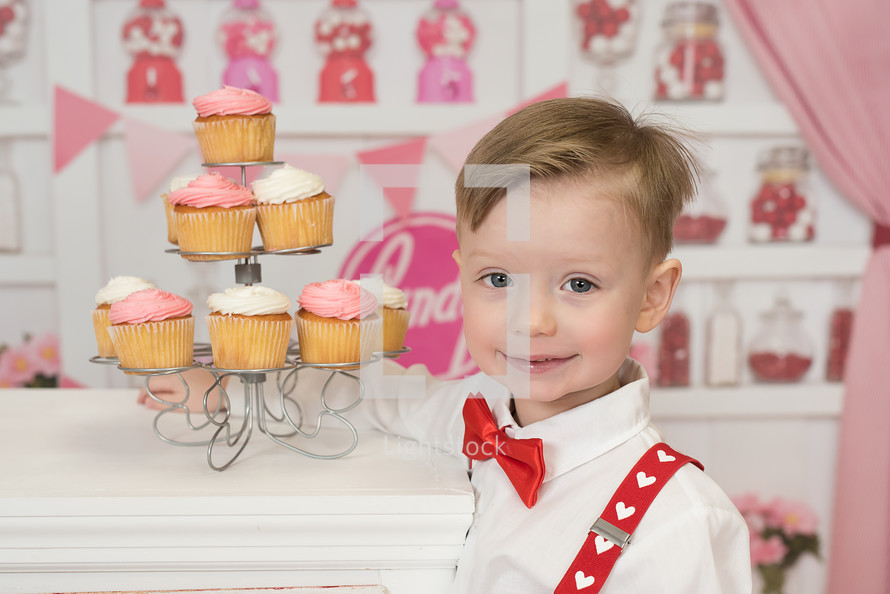 a boy standing beside a cupcake stand 