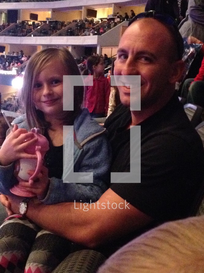 A father and toddler daughter sitting in a theater for Disney on Ice 