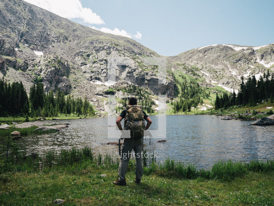 man with a backpack standing in front of a lake 