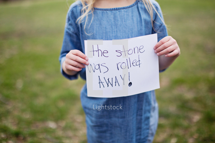girl holding a sign "the stone was rolled away"